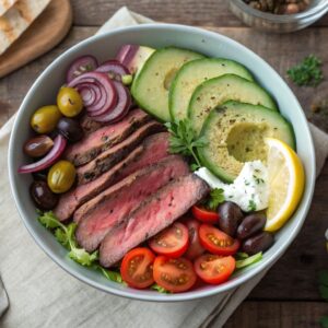 A vibrant Mediterranean steak bowl with sliced, juicy steak, cherry tomatoes, cucumbers, red onions, Kalamata olives, avocado, and a dollop of tzatziki sauce, drizzled with olive oil and garnished with fresh parsley. Served in a ceramic bowl on a rustic wooden table with a lemon wedge and pita bread on the side.